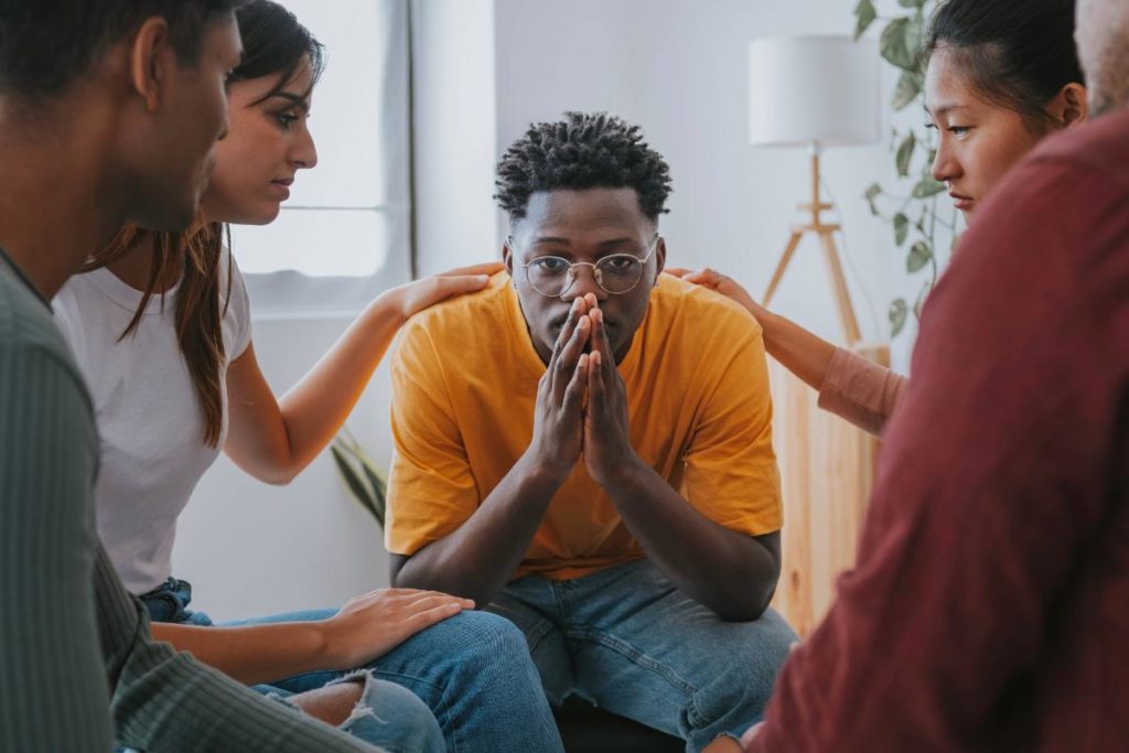 a group of people comforts a friend in a support group for recovering addicts