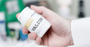 A professional holding a prescription bottle of Valium. The image is focused on the hand holding the bottle with the backdrop blurred out.