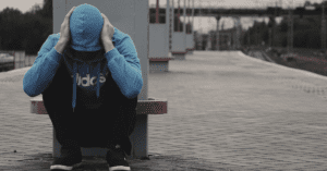 An addict wearing a hoodie and squatting at a train station