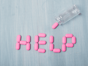 Pink prescription pills write the letter "help" out on a blue table.
