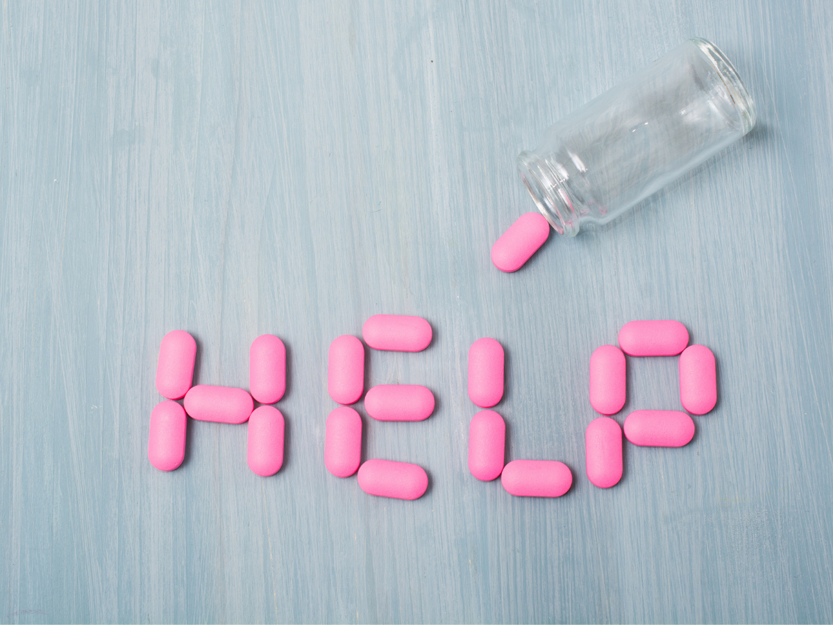 Pink prescription pills write the letter "help" out on a blue table.