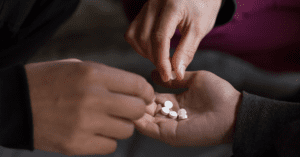 One open hand holding a palm full of pills as two other hands grab pills from the first hand