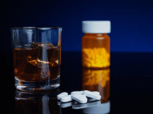 Glass of alcohol next to a prescription bottle and a pile of white pills.