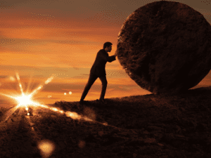 Man pushes a large ball up a hill while the sun sets.