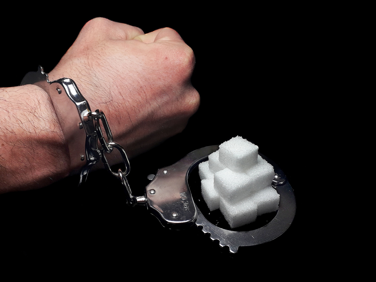 Man's hand is in police cuffs and the other half of the cuff is around cubes of sugar.