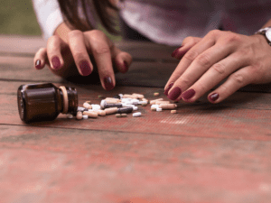 Woman's hands are shown while picking through pills that fell on the table.