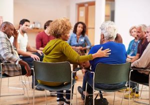 a large group of people sit in a circle in chairs while participating in a group therapy program