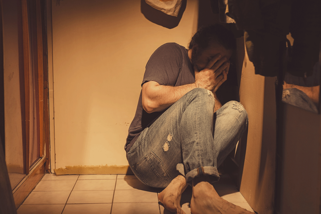 a person hides in a crawl space with shadows covering their face to show PTSD and addiction