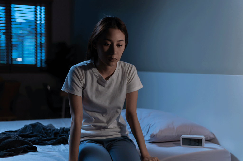 a woman sits in a dark bedroom to show bipolar symptoms in women