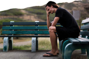 a man sits on a bench outside and shows signs of depression symptoms in men