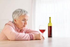 Senior person in brightly lit room drinking a glass of red wine while struggling with late onset alcoholism