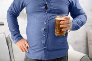Person holding mug of beer wearing blue button down shirt that is too tight before dealing with gastric bypass and alcoholism