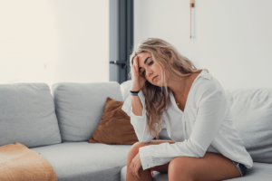 Woman sighs and sits on couch while wondering what self-medication is