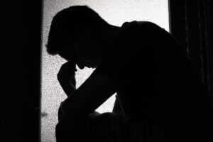 Man leans on self in the dark, wondering "is addiction a disease?"